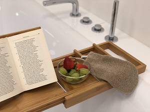 Badewannentablett mit Buch, Massagehandschuh und Obst