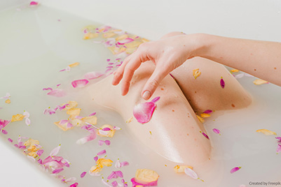 Knie einer Frau in der Badewanne mit Wasser und Blütenblättern