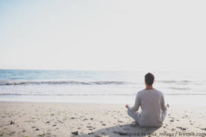 Junger Mann meditiert am Strand