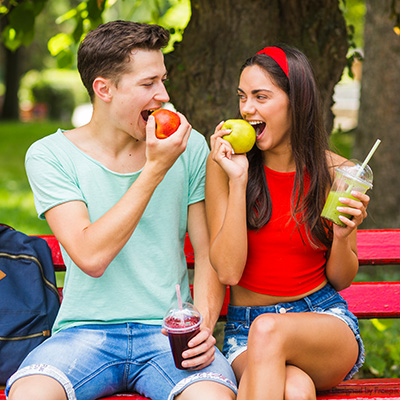 Junges Paar auf der Parkbank mit Apfel und Smoothie